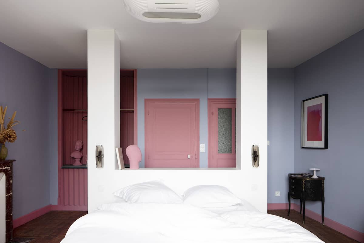 A bedroom with a large bed, a pink door, and a small table with a lamp.
