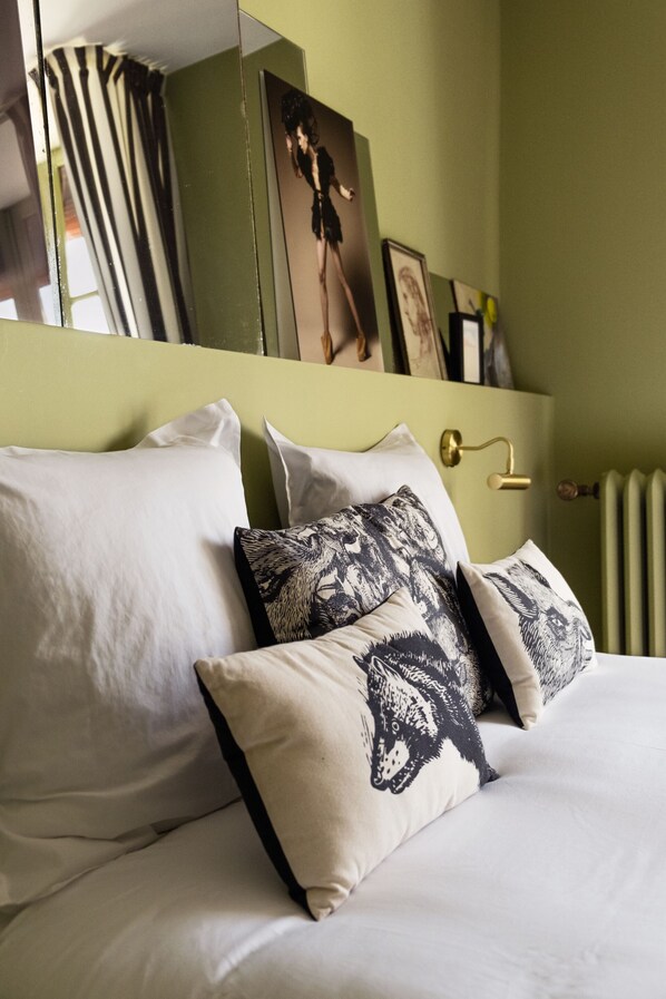 Un lit bien fait, avec des oreillers blancs et à motifs, un mur vert et un tableau encadré au-dessus du lit.