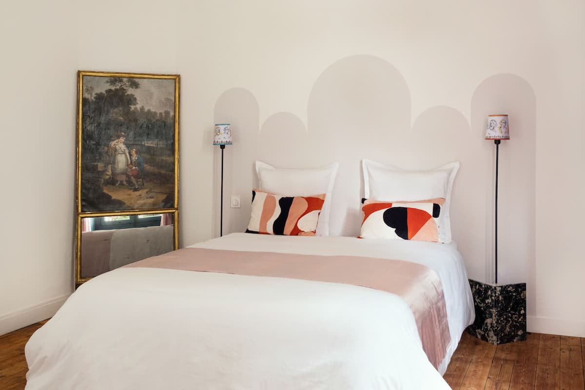 A bedroom with a bed, a painting, and two floor lamps.