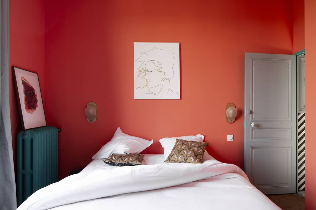 A bedroom with a red wall, white bedding, and a door with a striped pattern.