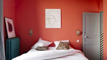 A bedroom with a red wall, white bedding, and a door with a striped pattern.