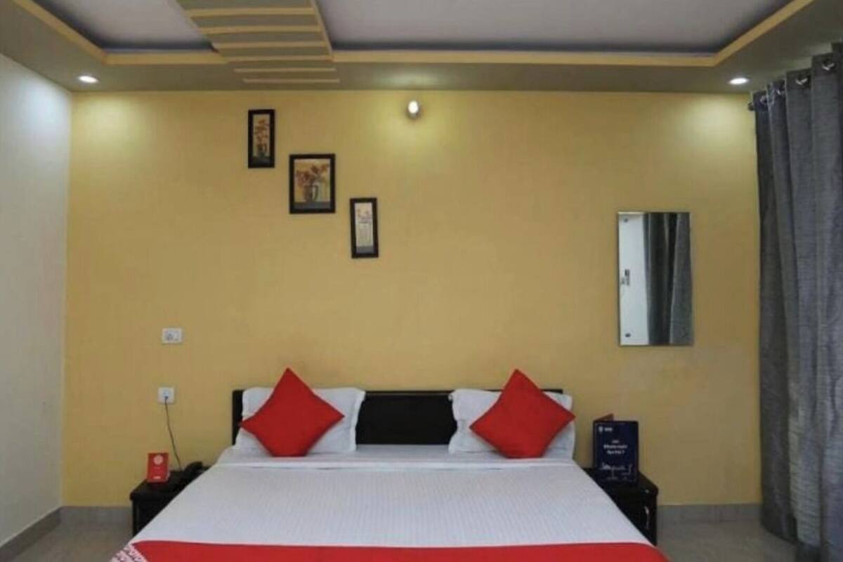 Una habitación de hotel con cama, mesita de noche, televisor montado en la pared y ventilador de techo.