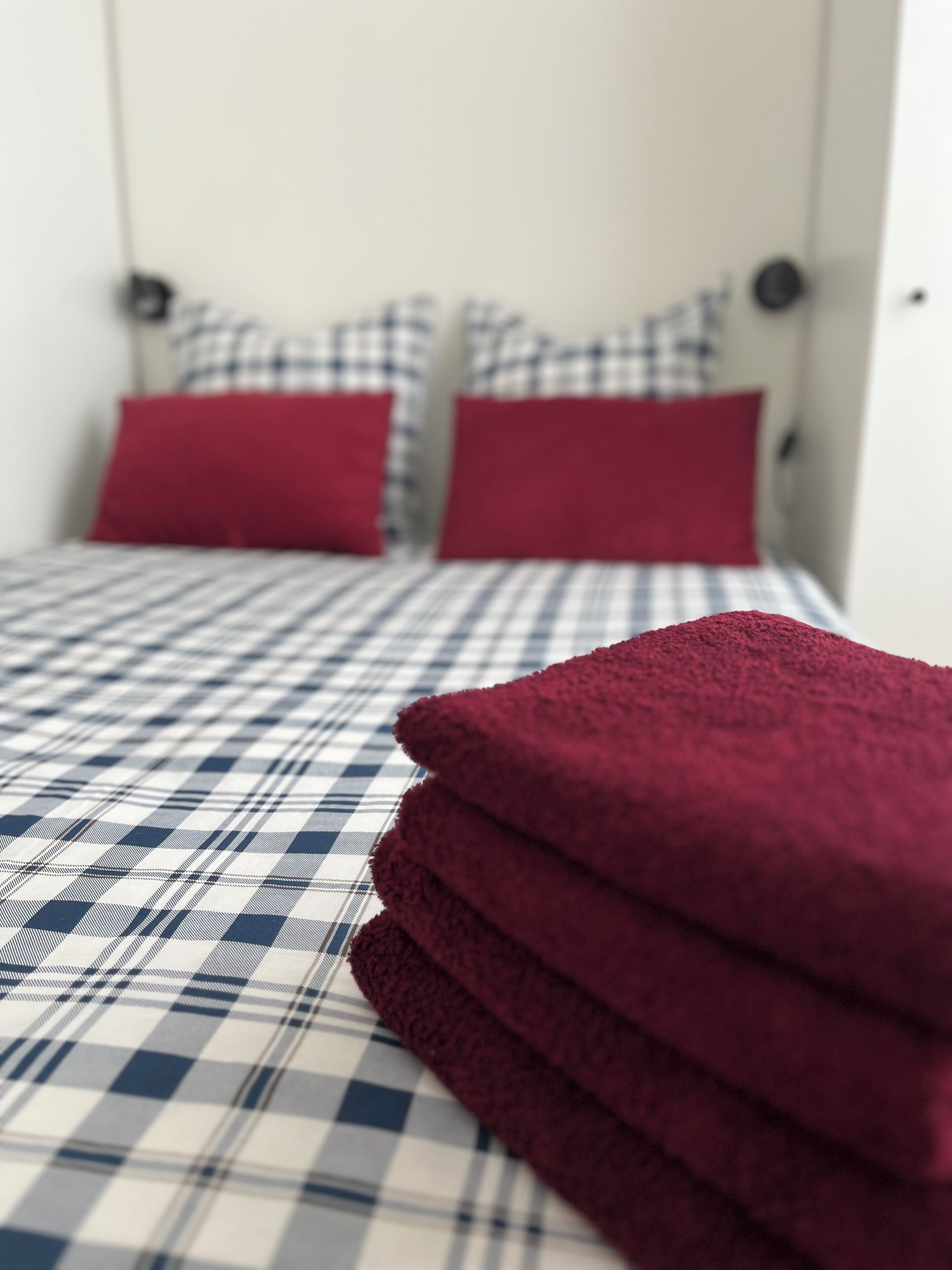 Ein Bett mit einer karierten Tagesdecke und zwei roten Kissen.