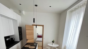 A modern kitchen with white cabinets, a black countertop, and a central island. There is a dining area with a white table and chairs, and a gray sofa with a patterned pillow. - Cosy apartment 1 min from Paris (Charenton-le-Pont)
