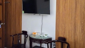 A hotel room with a wooden wardrobe, a flat-screen TV mounted on the wall, a round table with chairs, and a small side table with a bottle and a glass. - A10 Thuy Hoa Hotel LC  - by BAY LUXURY (Lao Cai)