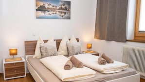 A neatly made bed with pillows and towels, a bedside table with a lamp, a wall-mounted picture, and a window with curtains. - Farmhouse in Hollersbach with Mountain Views (Hollersbach im Pinzgau)
