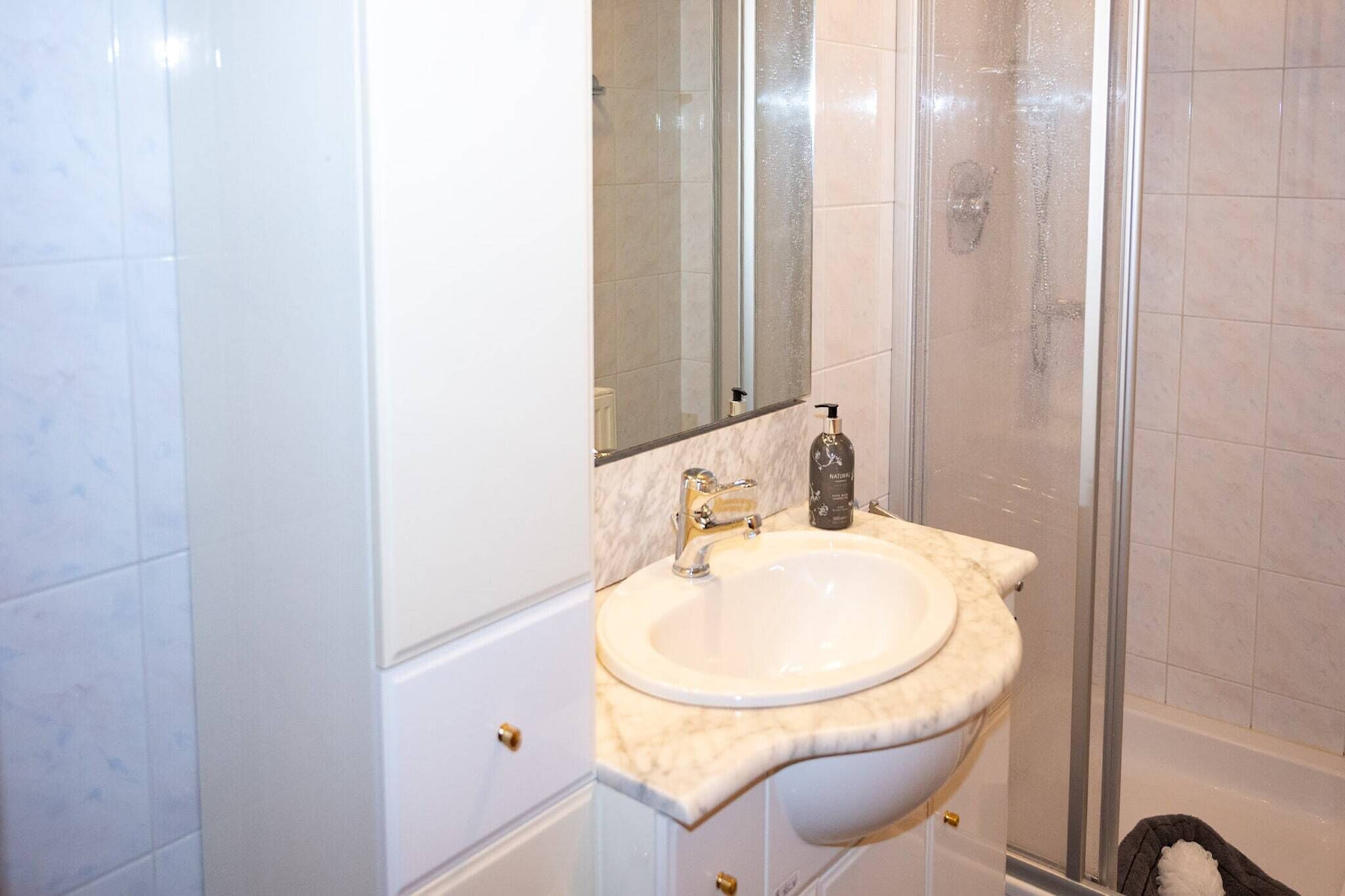 A bathroom with a white sink, a mirror, and a shower enclosure.