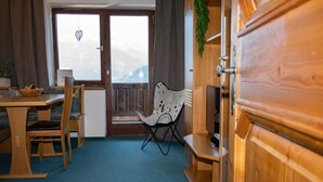 A room with a wooden dining table and chairs, a folding chair, a television, and a view through a glass door. - Farmhouse in Hollersbach with Mountain Views (Hollersbach im Pinzgau)