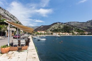 A waterfront terrace with outdoor seating, boats, and a mountainous backdrop. - 2 bedroom apartment with Sea view (Trstenik)