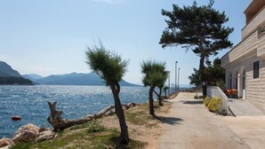 A coastal pathway with a building on the right, overlooking a body of water and mountains. - Apartments Bezek - Studio Apartment with Sea View (Trstenik)