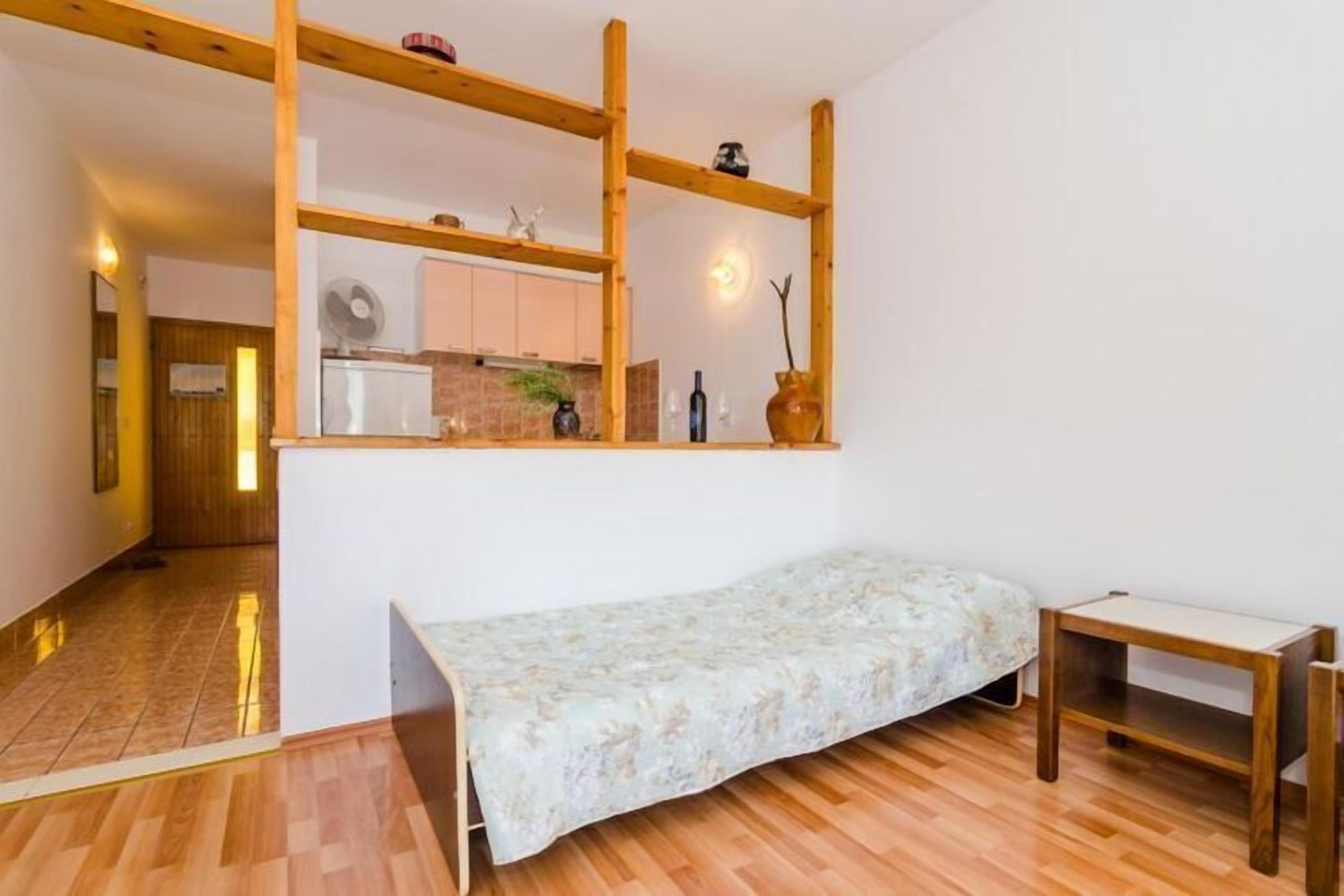 A compact room with a bed, a small table, and a wooden shelf unit above the bed.
