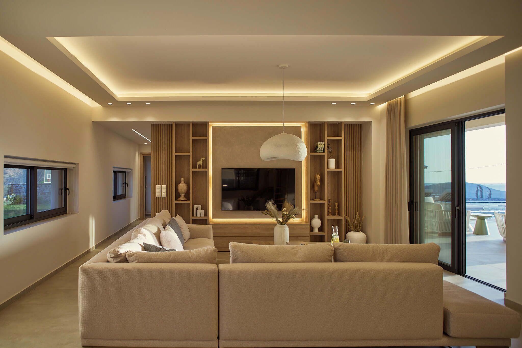 A modern living room with a large sofa, a flat-screen TV, and a view of the outdoors.
