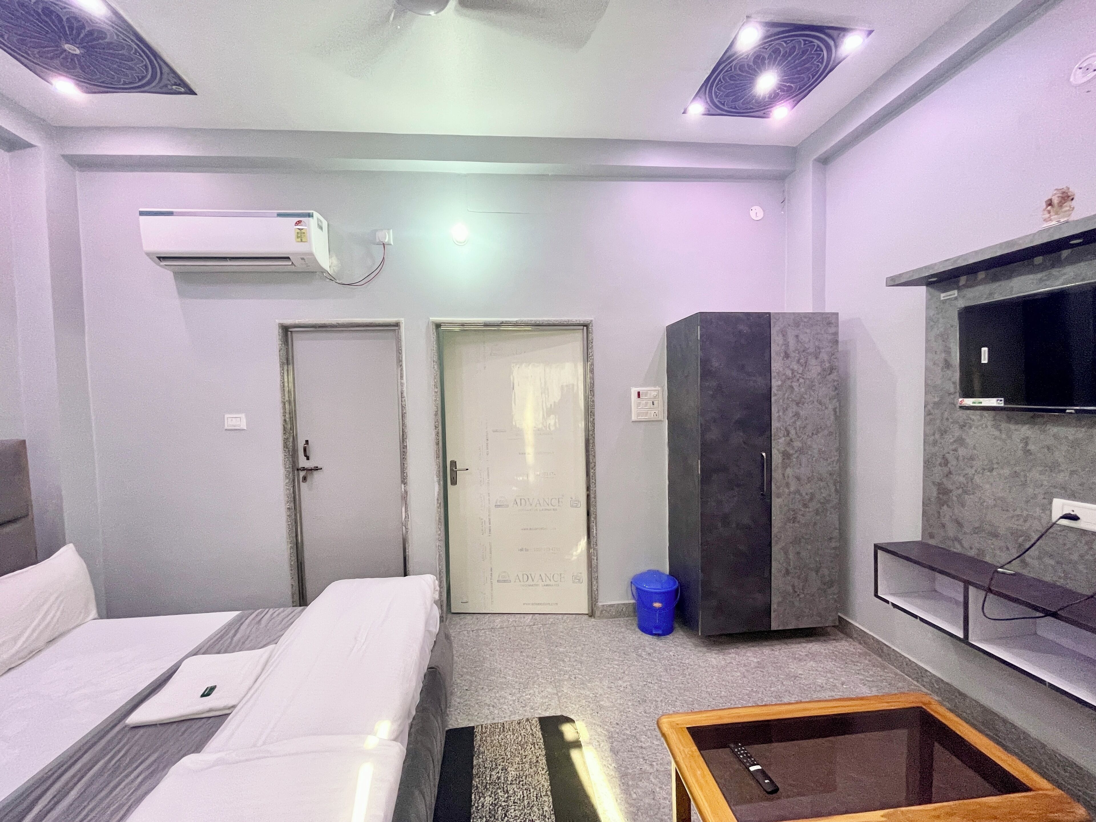 A hotel room with a bed, a desk, a wardrobe, a TV mounted on the wall, and an air conditioning unit.