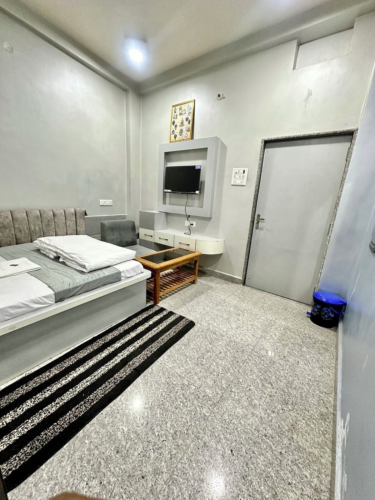 A modern bedroom with a bed, a TV mounted on the wall, a small table, and a door.