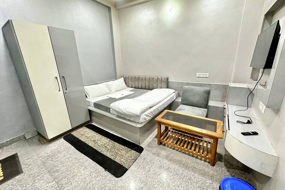 A compact hotel room with a bed, a desk, a chair, a wardrobe, and a small table.