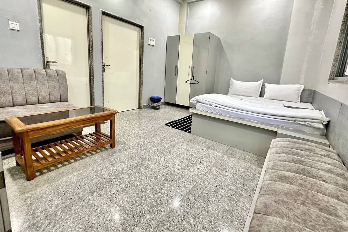 A compact hotel room with a sofa, a bed, a wooden coffee table, and a wardrobe.