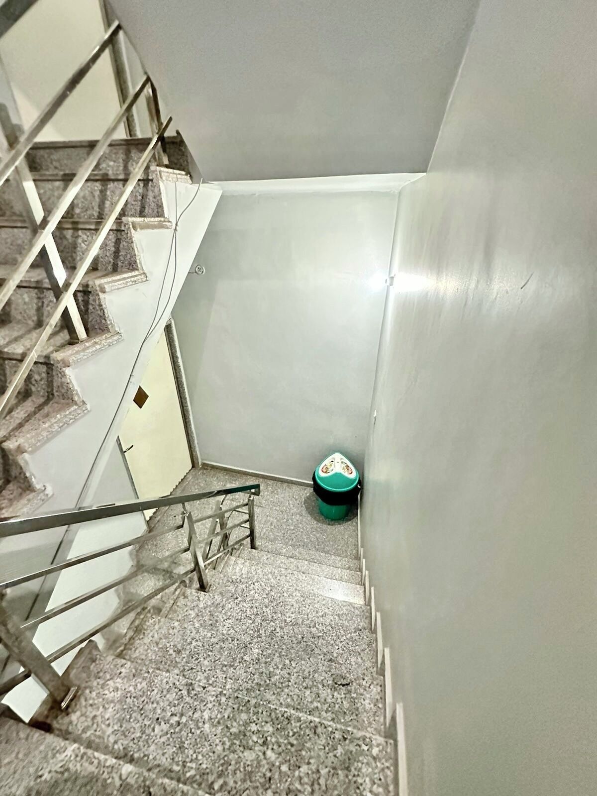 A staircase with metal railings and a green trash bin at the bottom.