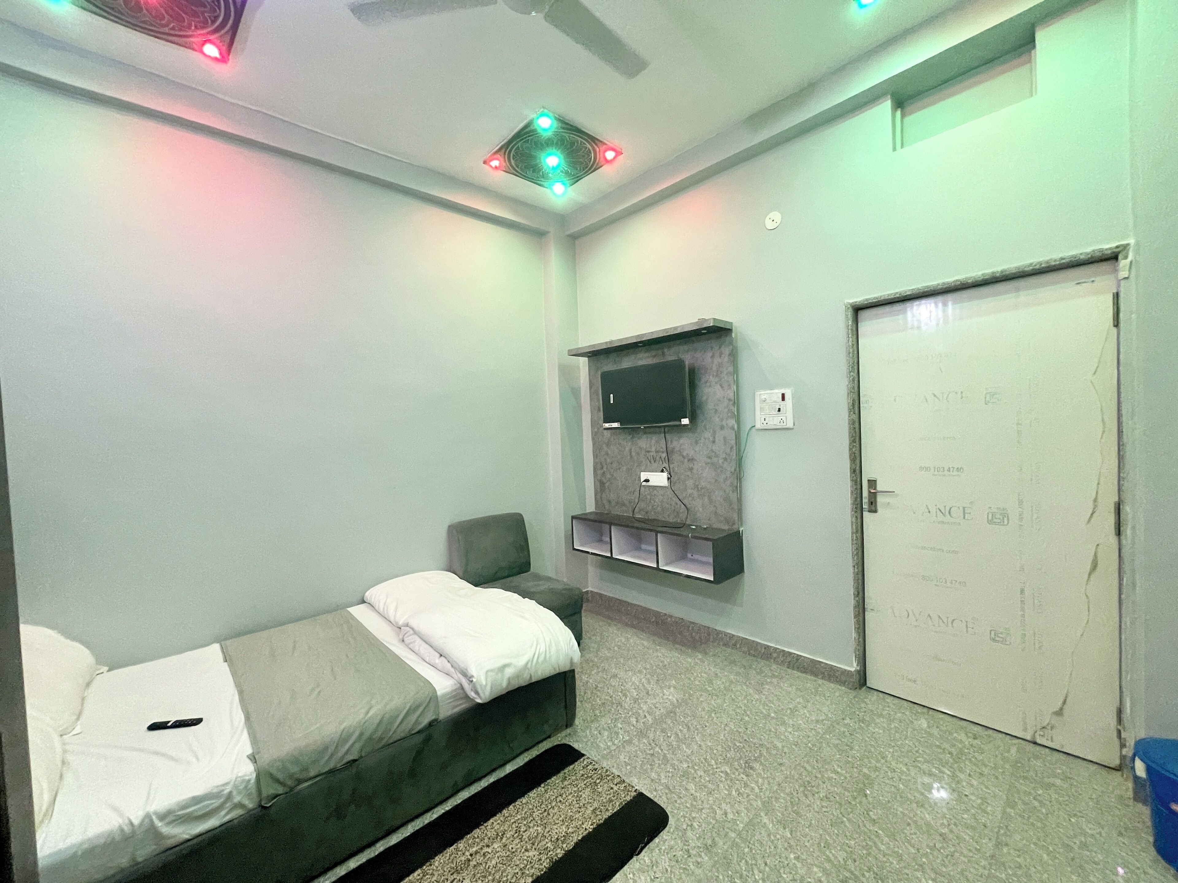 A small, neatly arranged room with a bed, a television mounted on the wall, and a door with a sign.