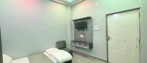 A small, neatly arranged room with a bed, a television mounted on the wall, and a door with a sign.