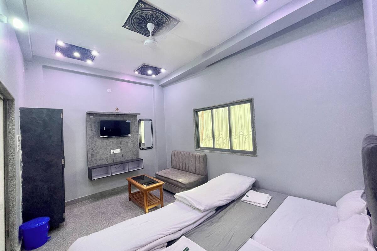 A hotel room with a bed, a TV mounted on the wall, a small table, and a window with curtains.