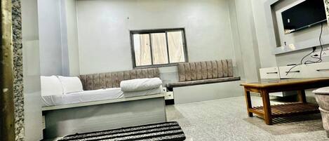 A compact room with a bed, a bench, a small table, and a TV mounted on the wall.