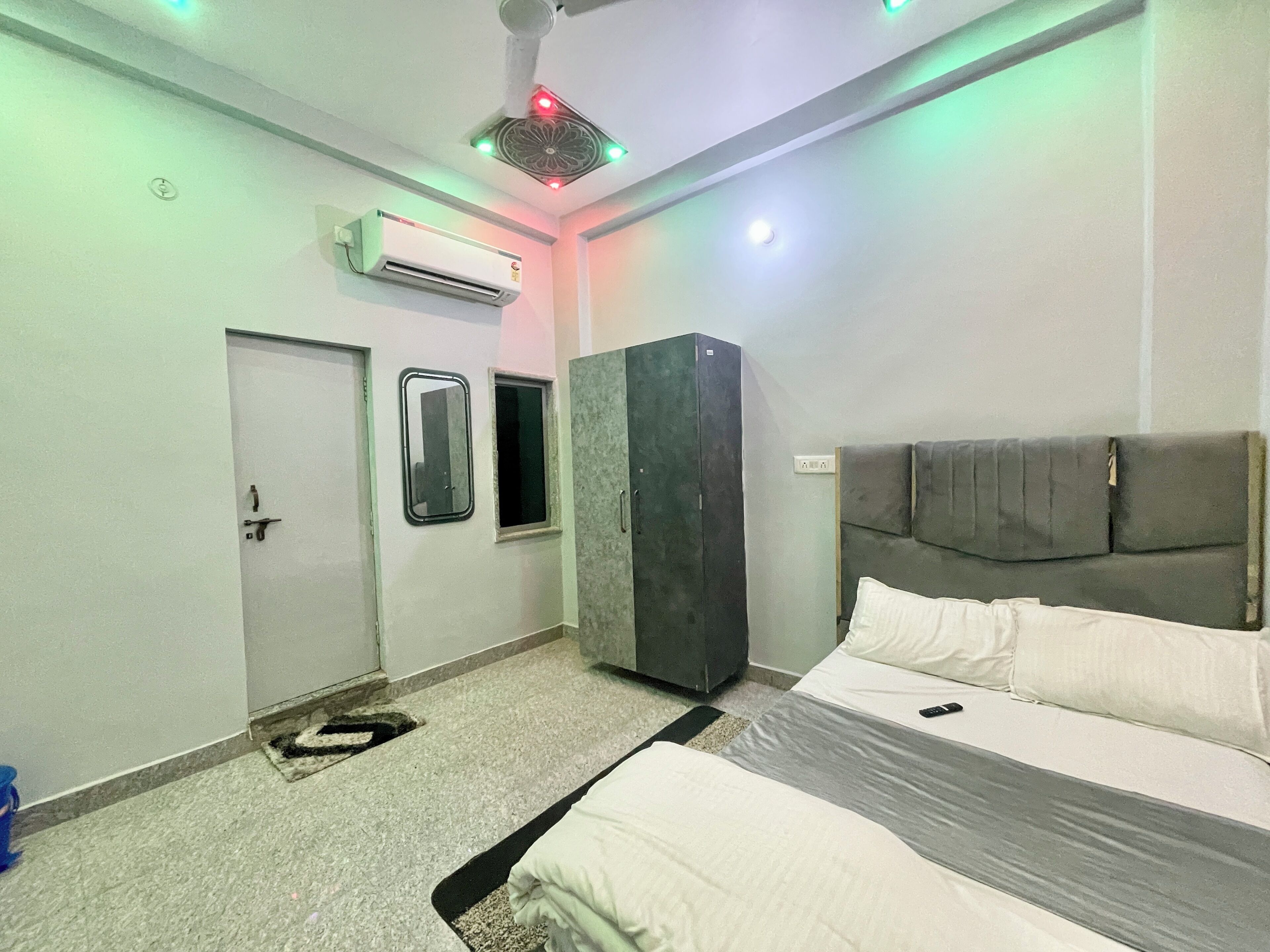 A bedroom with a bed, a wardrobe, an air conditioning unit, a door, and a small window.