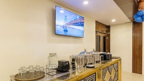 A hotel reception area with a flat-screen TV displaying a bridge, a counter with various amenities, and a decorative wall panel. - Treebo AR Grand, Gajuwaka (Visakhapatnam)