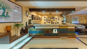 A hotel reception area with a modern design, including a reception desk, a wall with framed pictures, and a logo on the counter. - Treebo AR Grand, Gajuwaka (Visakhapatnam)