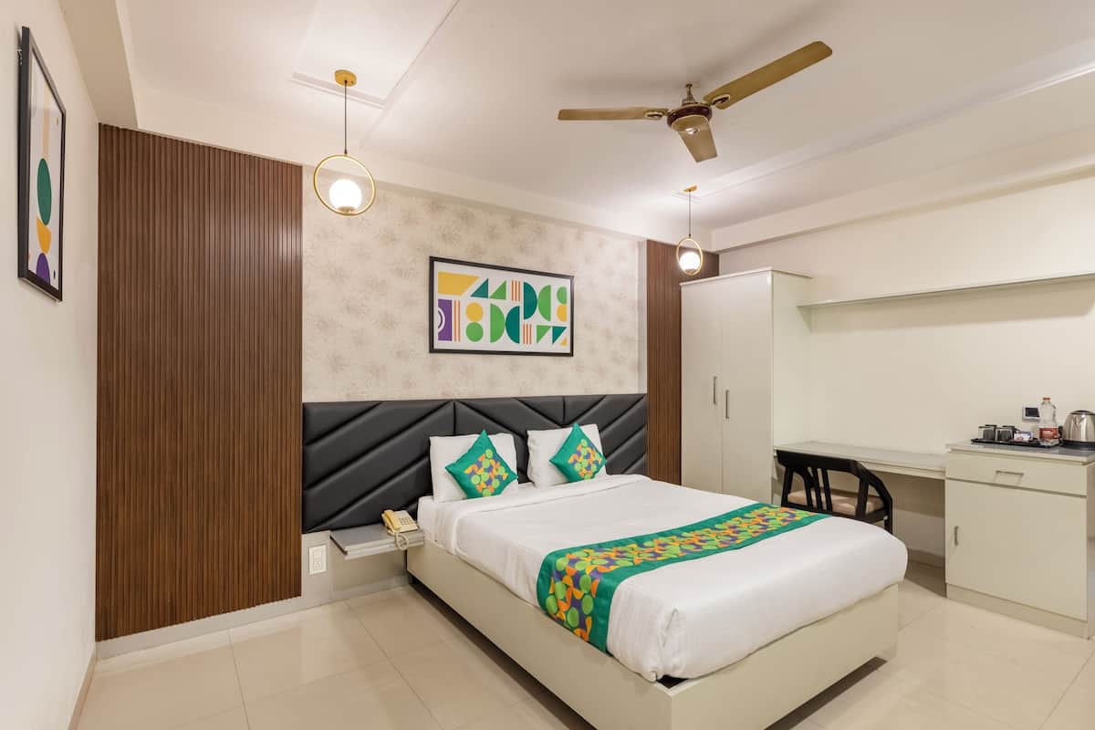 A modern hotel room with a bed, a desk, a chair, a ceiling fan, and a wall-mounted artwork.