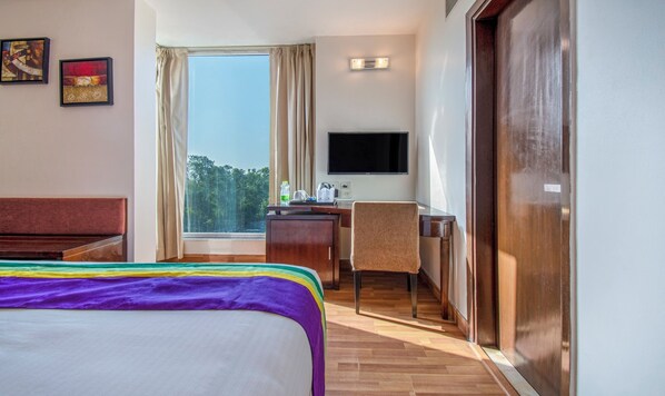 A hotel room with a bed, desk, chair, TV, and a window with curtains. - Treebo AR Grand, Gajuwaka (Visakhapatnam)