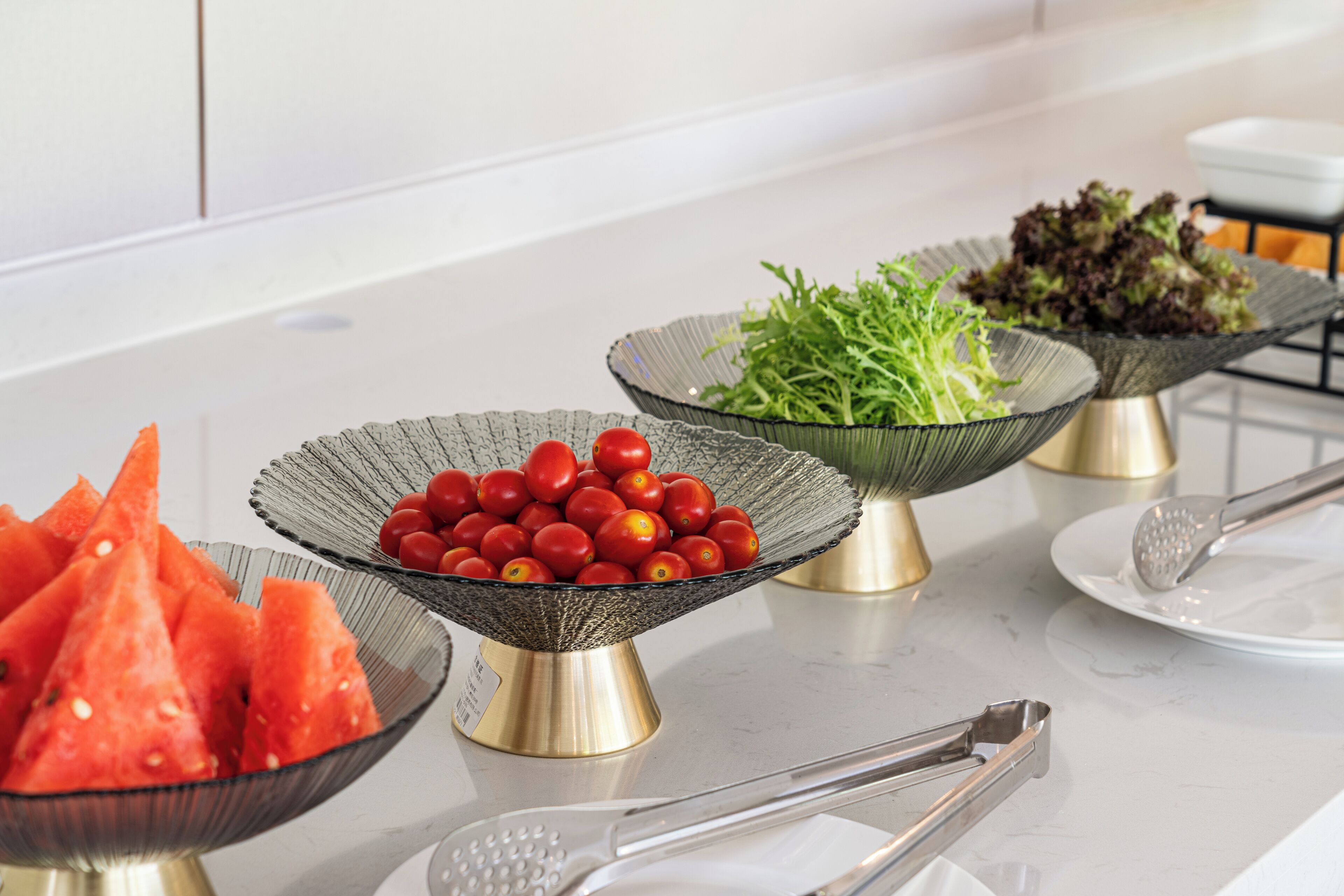 A buffet table with various food items including watermelon, tomatoes, and greens.