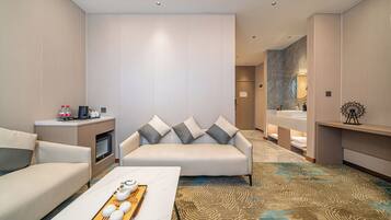 A modern hotel room with a sofa, a coffee table with a tray of eggs, a TV, and a bathroom with a mirror and sink.