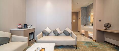 A modern hotel room with a sofa, a coffee table with a tray of eggs, a TV, and a bathroom with a mirror and sink.