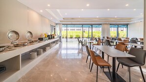 Un vaste espace dédié à la salle à manger, avec de nombreuses tables et chaises, un buffet proposant une variété de plats, et de grandes fenêtres offrant une vue sur la verdure environnante.