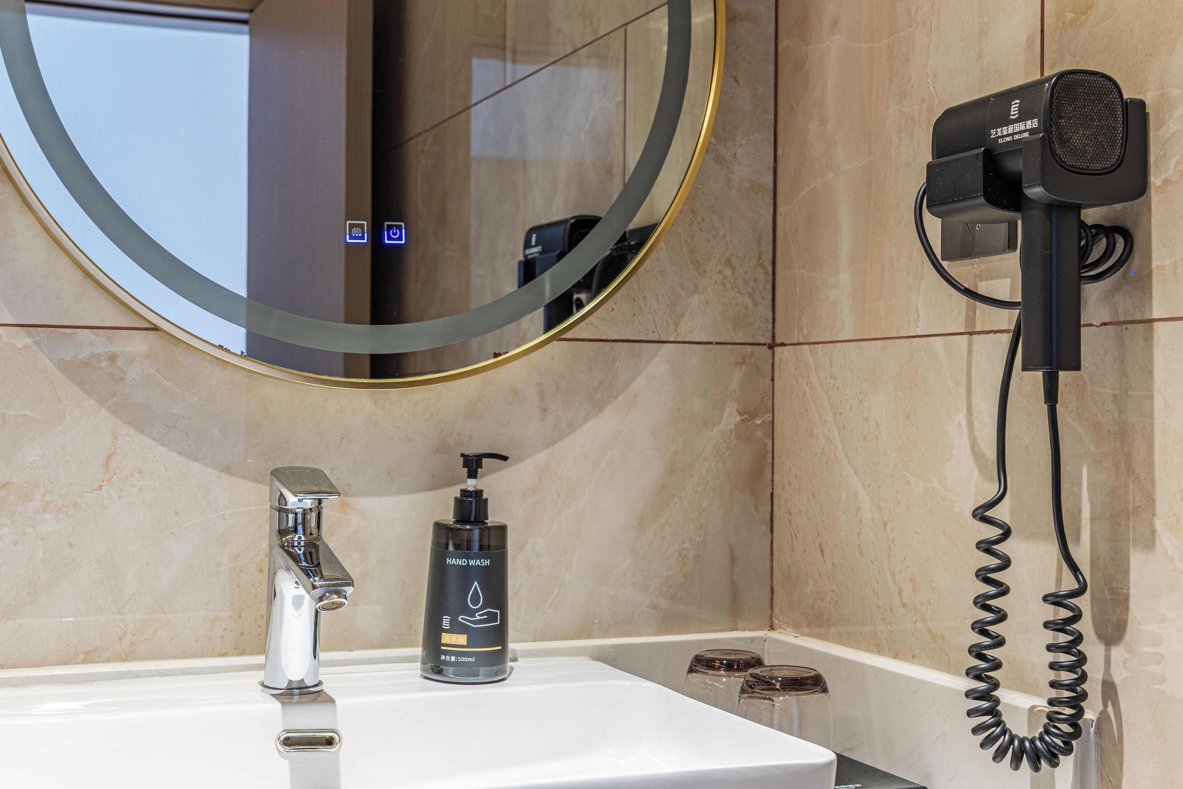 A bathroom with a sink, hand wash dispenser, and a hair dryer mounted on the wall.