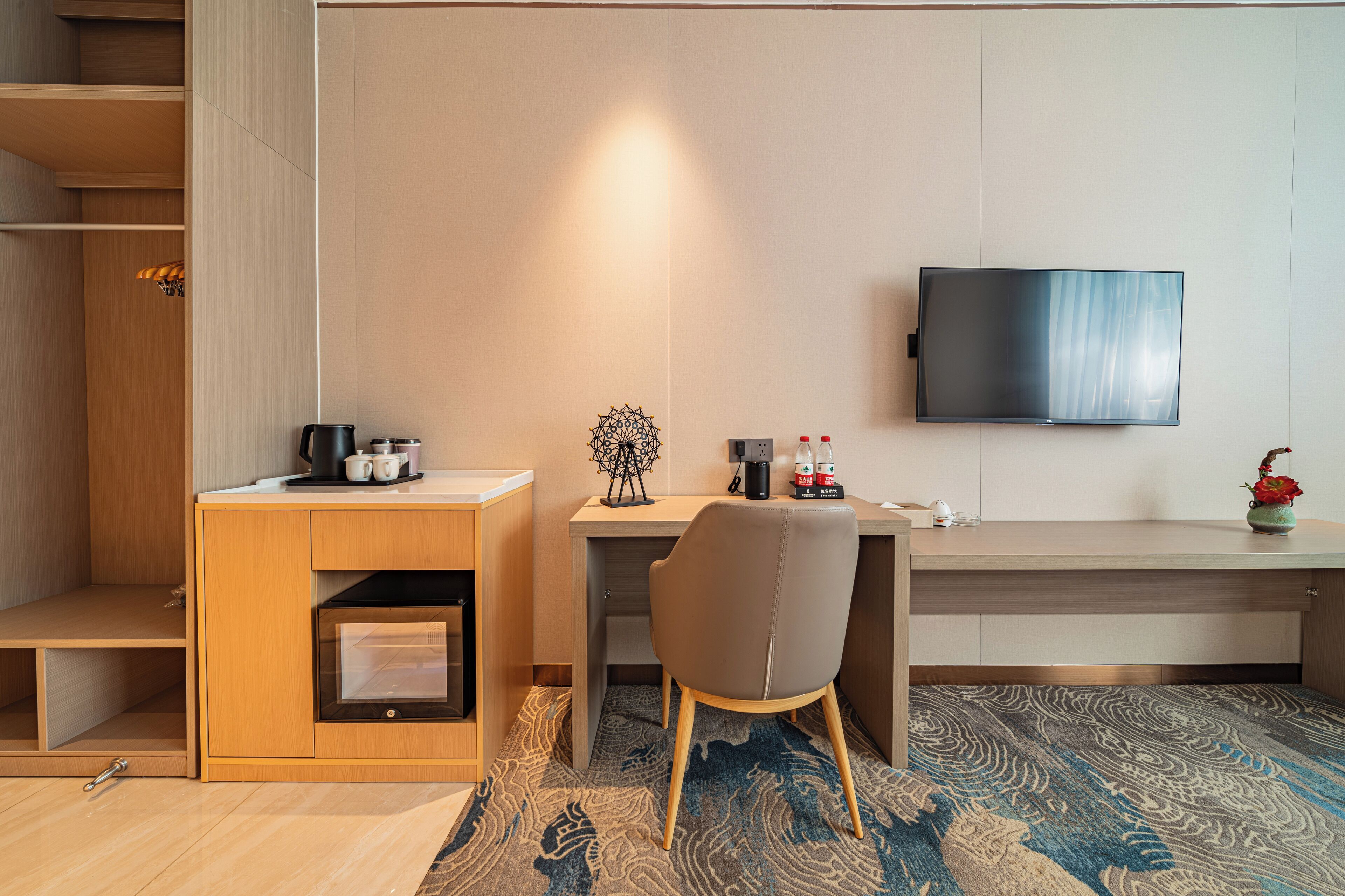 Habitación de hotel pequeña y funcional con escritorio, silla, televisor y una kitchenette.
