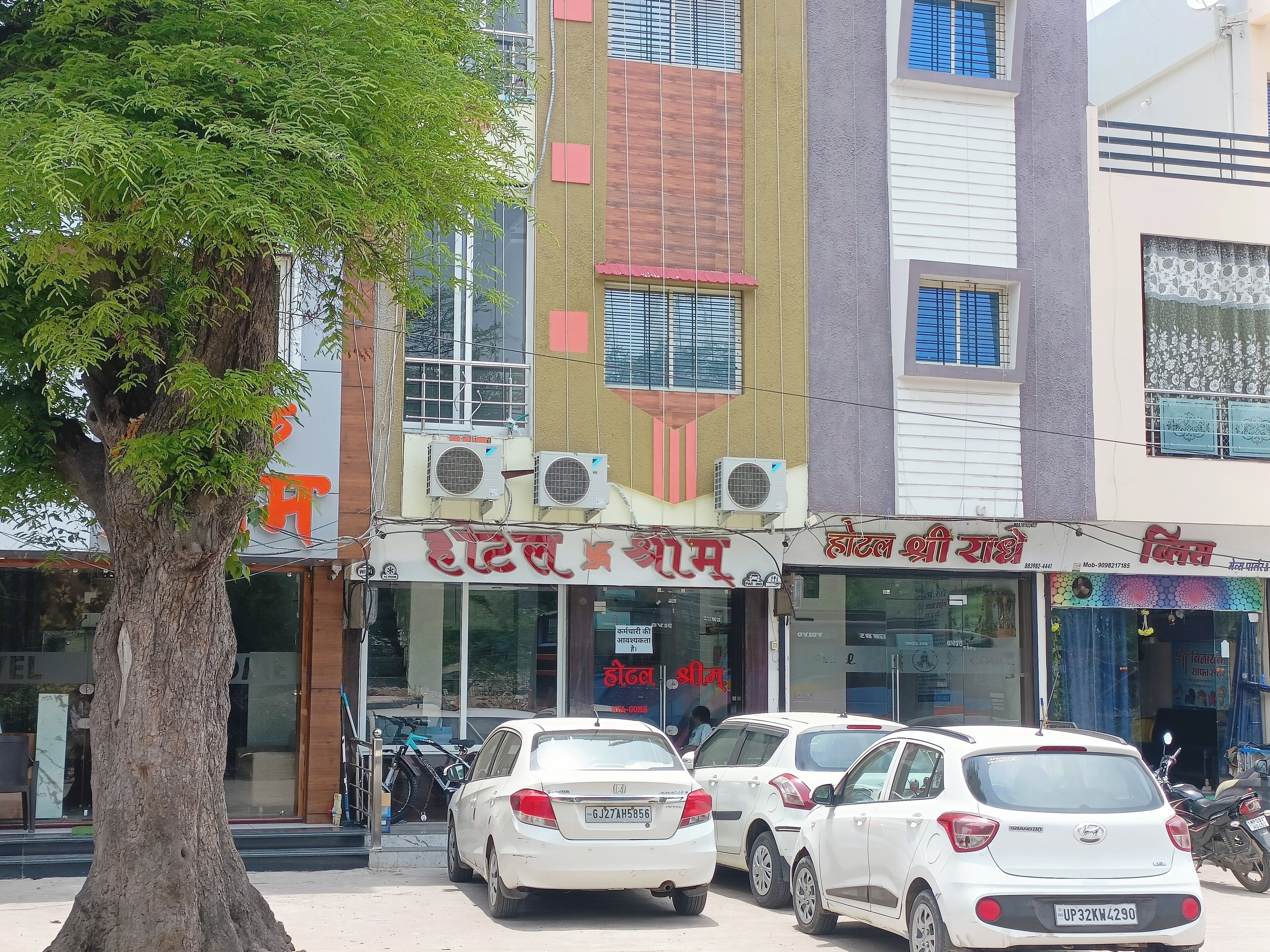 A building with multiple shops on the ground floor, including a hotel and a restaurant. There are several parked cars in front.