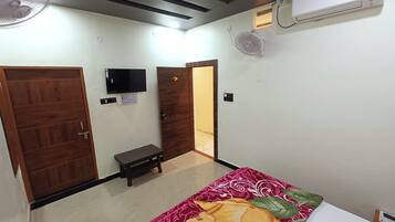 A hotel room with a bed, two doors, a small table, a TV, an air conditioner, and a ceiling fan.