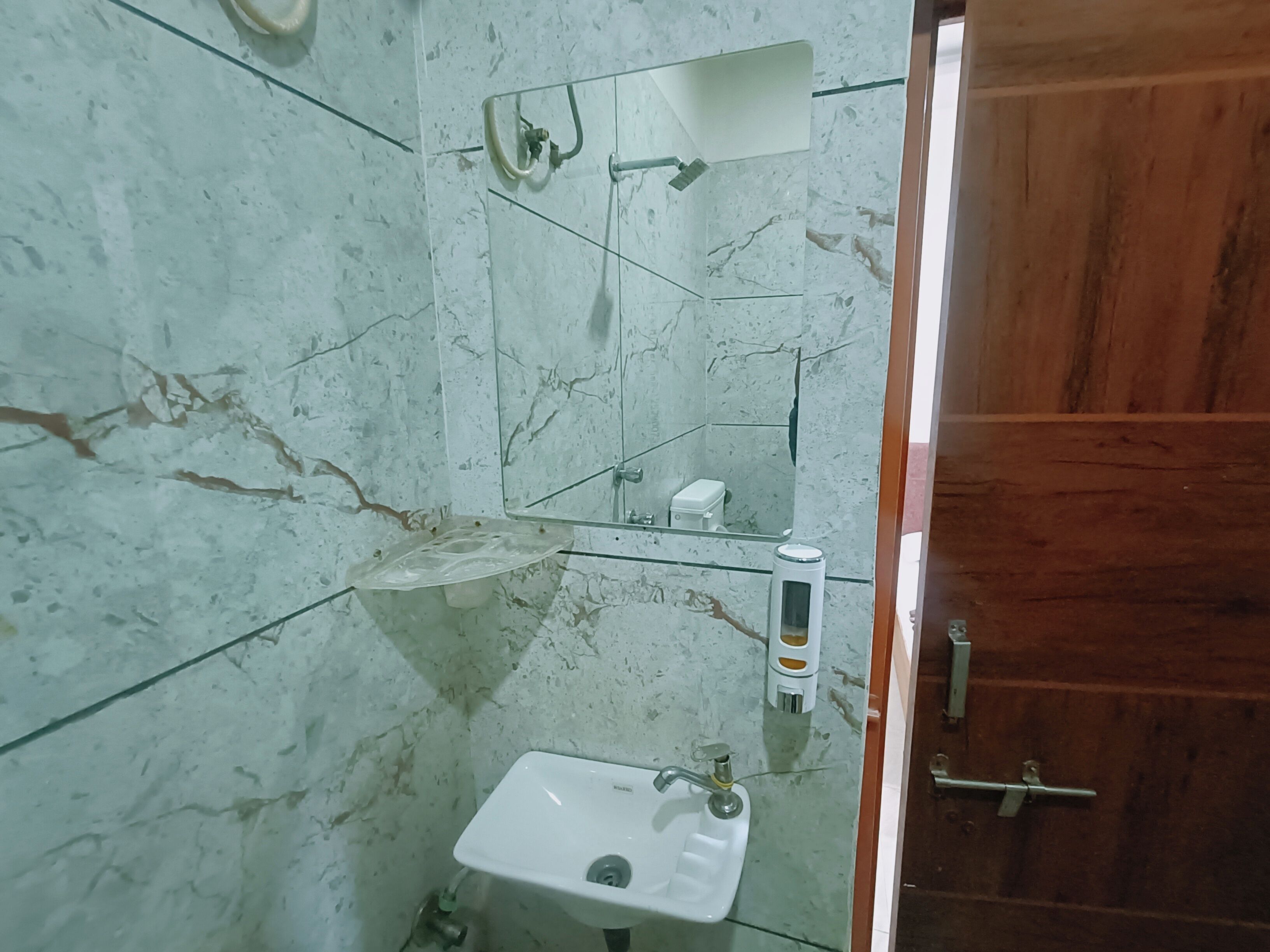 A bathroom with a marble floor, a white sink, a glass shower enclosure, and a wooden door.
