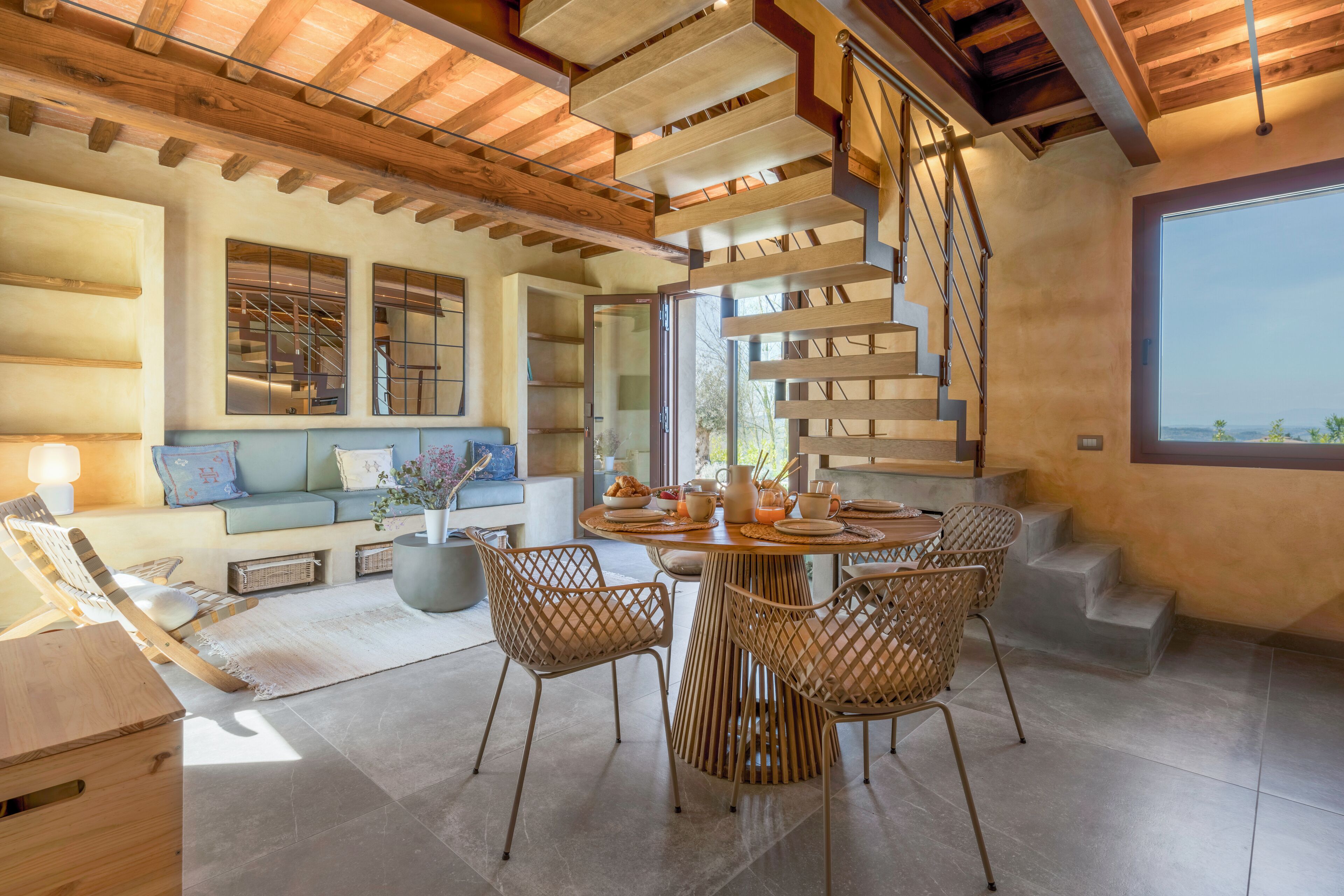 A modern interior with a wooden ceiling, a spiral staircase, a round dining table with chairs, and a large window.