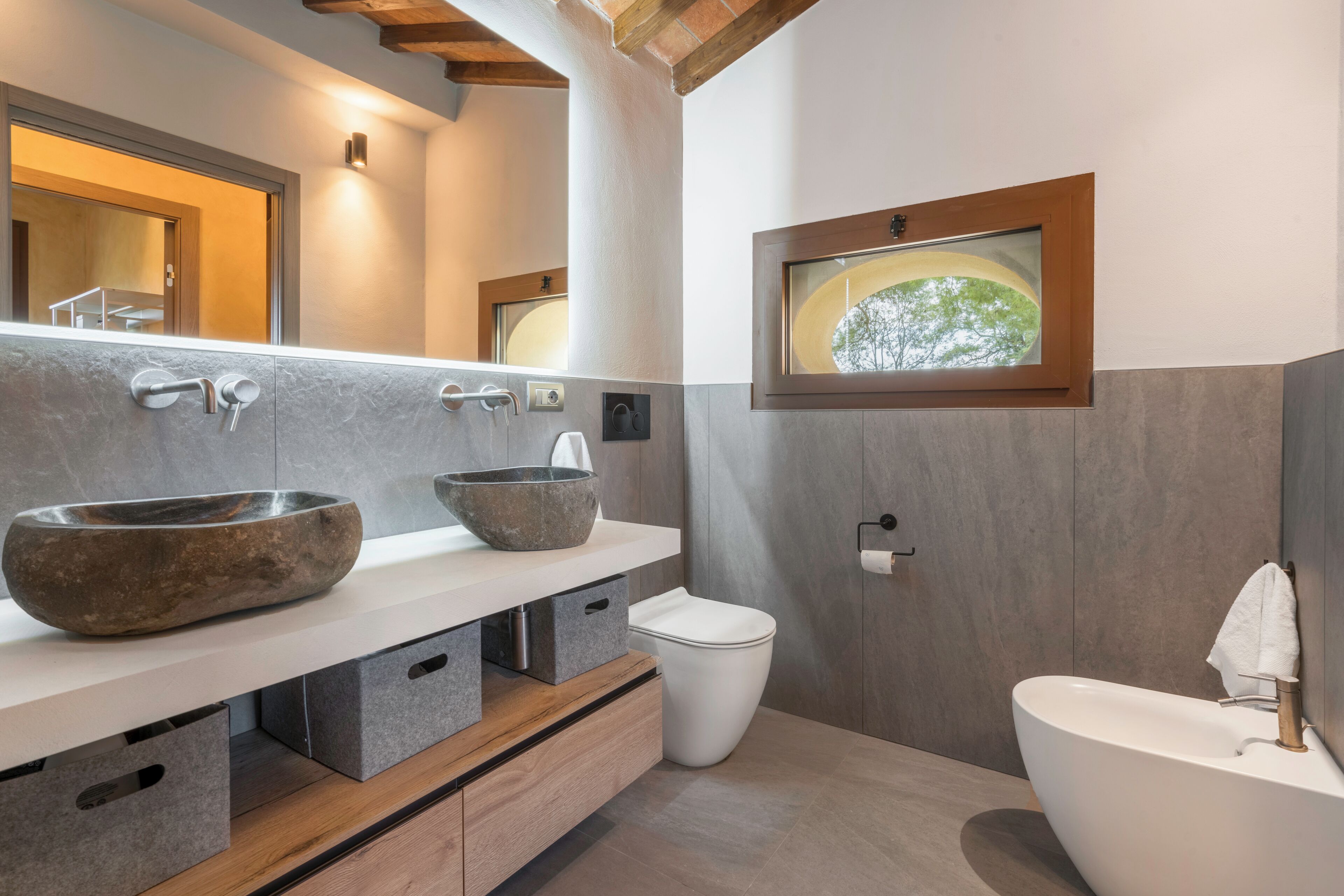 Et moderne badeværelse med en stor sten-vask, et toilet og et badekar. Der er et træskab under vasken og et billede i ramme på væggen.
