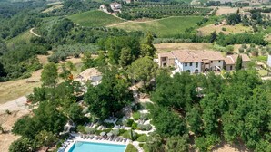 An aerial view of a property with a swimming pool surrounded by lush greenery, a large white building with a tiled roof, and vineyards in the background. - Punteriolo Family Apartment, Nice Garden Pool Montaione (Montaione)