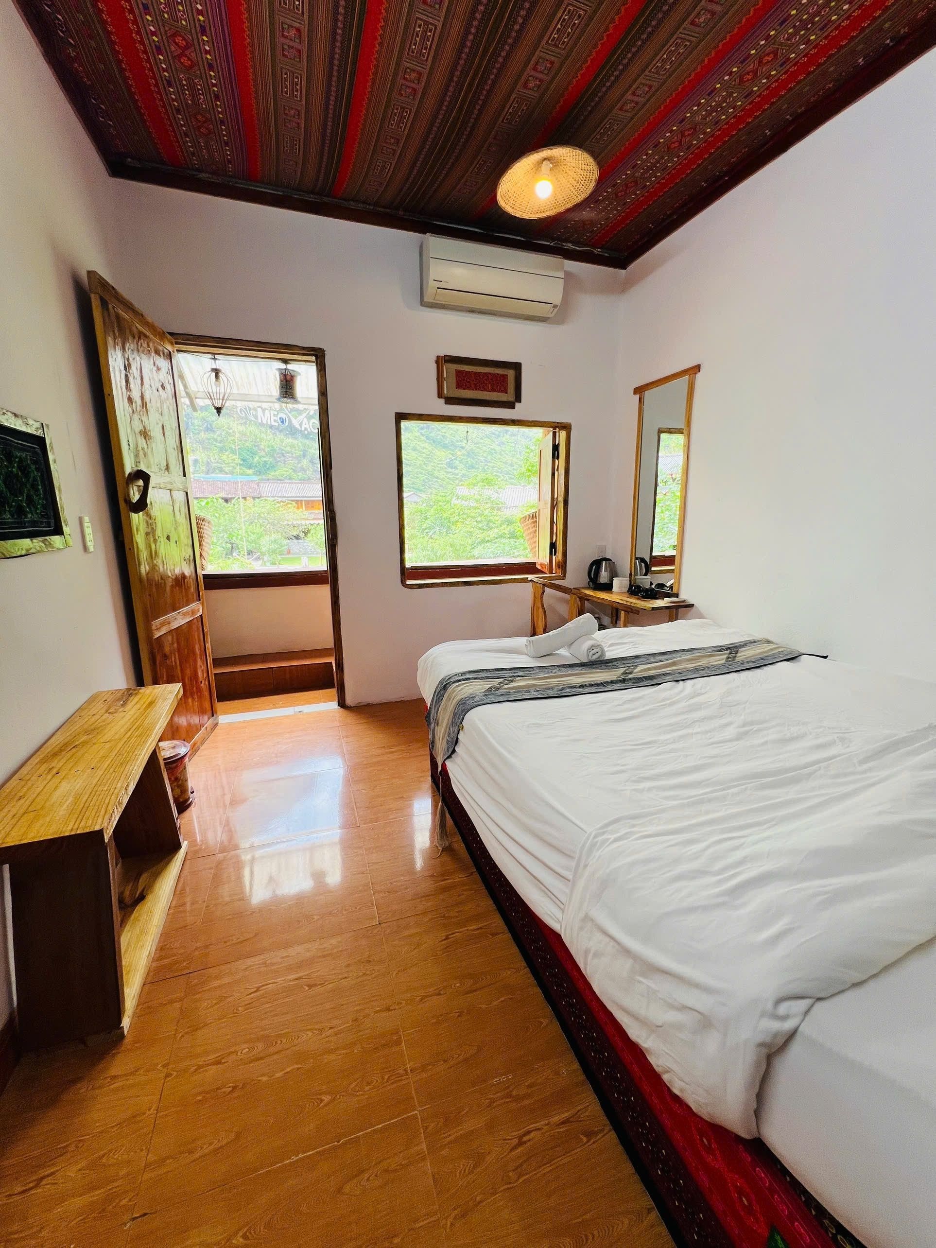 Quarto com cama, um banco de madeira, janela e espelho.