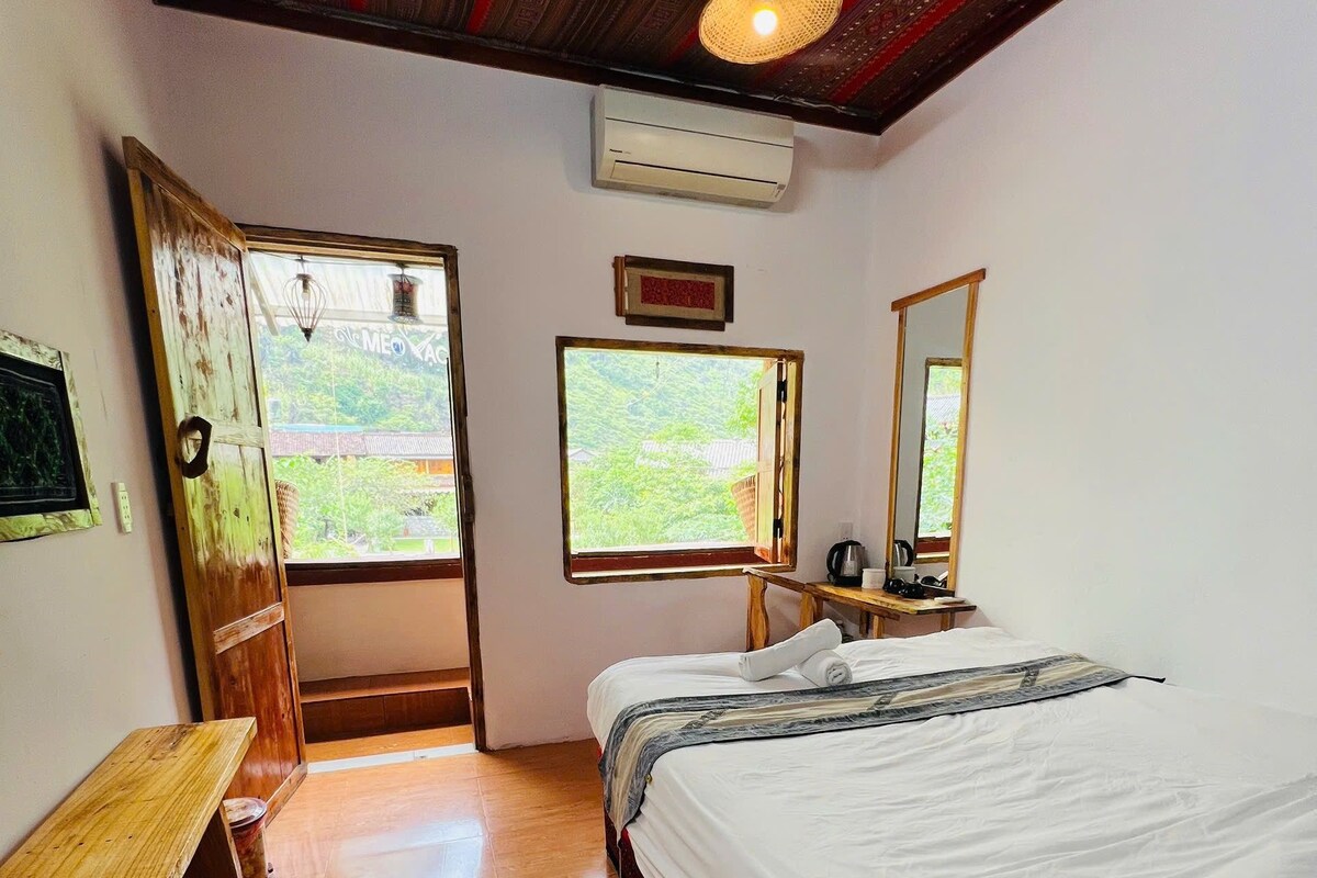 Una habitación con una cama, un banco de madera, un ventanal y un espejo.