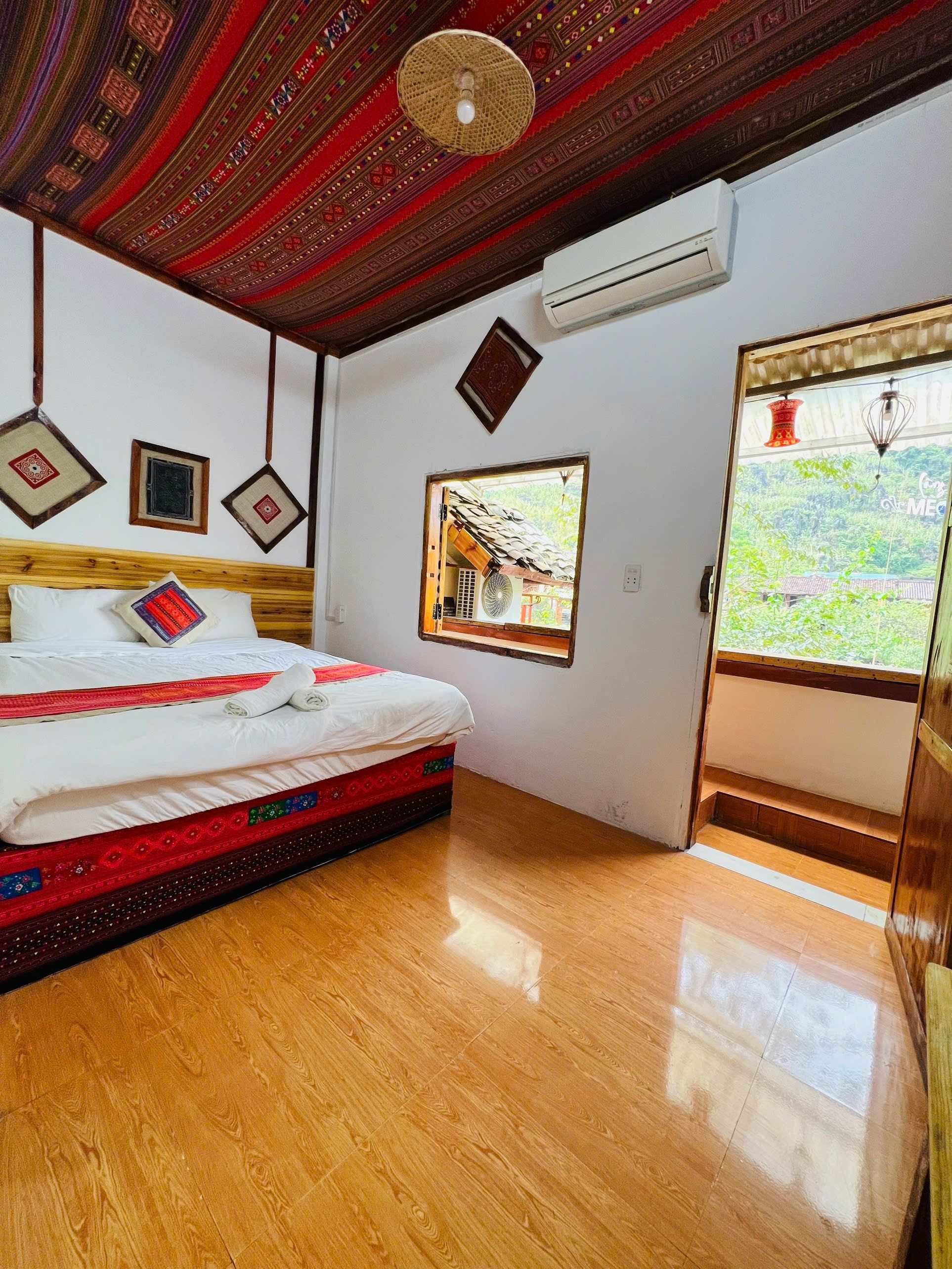 Una habitación con una cama de madera, aire acondicionado en la pared y ventana con vista a follaje.