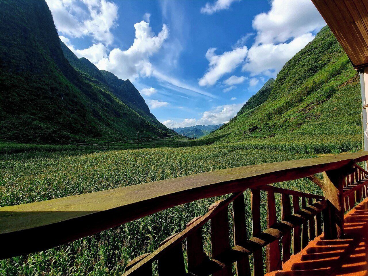 A wooden deck overlooking a lush valley with mountains in the background.