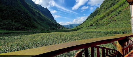 A wooden deck overlooking a lush valley with mountains in the background.
