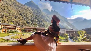 A person in traditional attire sitting on a balcony with a mountainous landscape in the background. - O'Chau Meo Vac Homestay (Meo Vac)