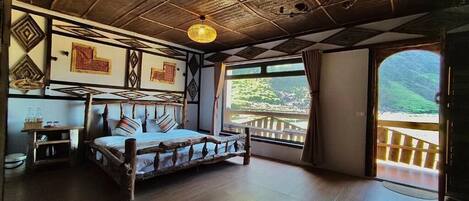 A rustic room with a wooden bed, a hanging light fixture, and a view of a balcony with a wooden railing.