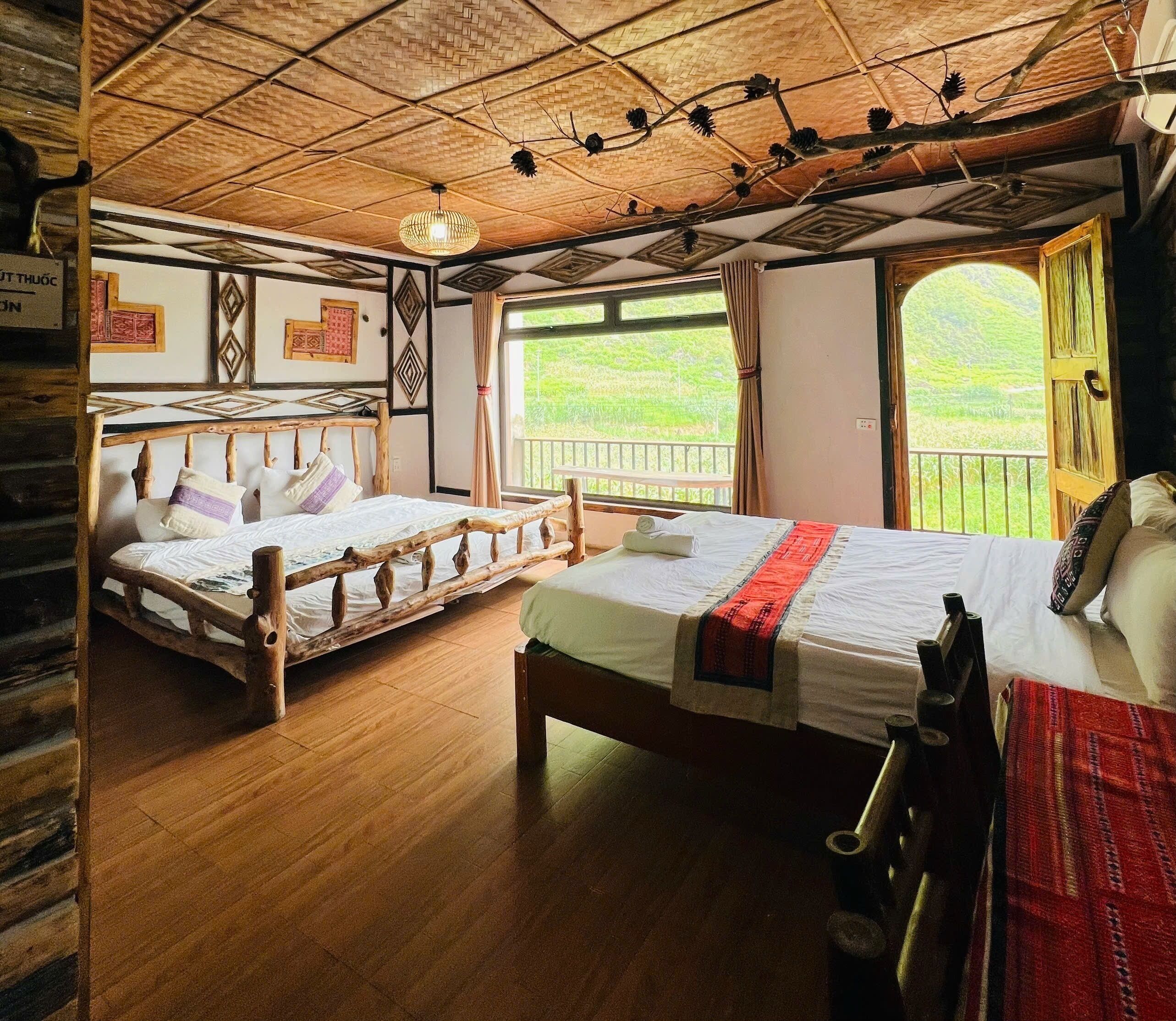 A room with two wooden beds, a woven ceiling, and a balcony with a view of greenery.